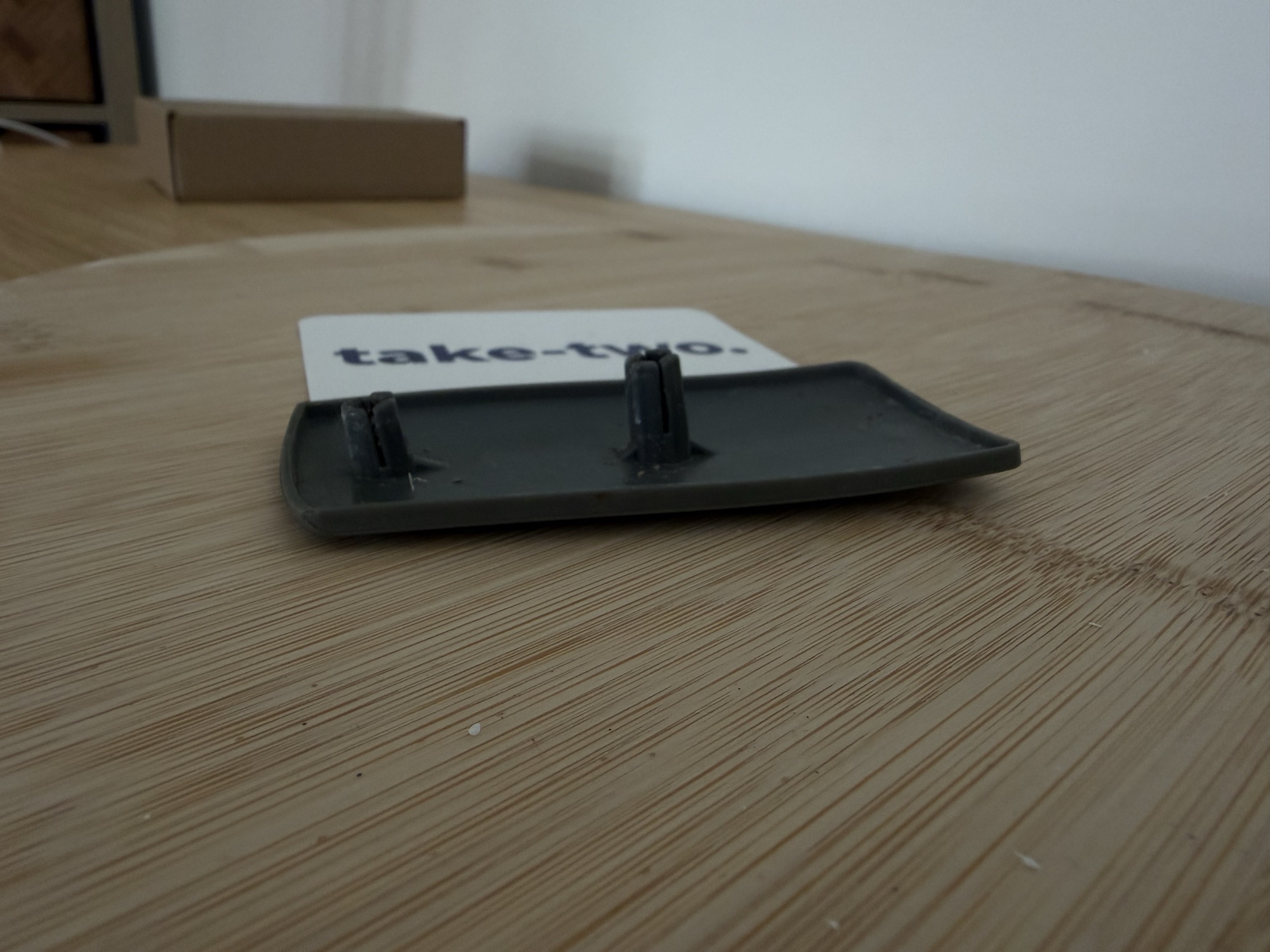 A dark grey plastic end cap with two clip posts, photographed on a wooden turntable before scanning.