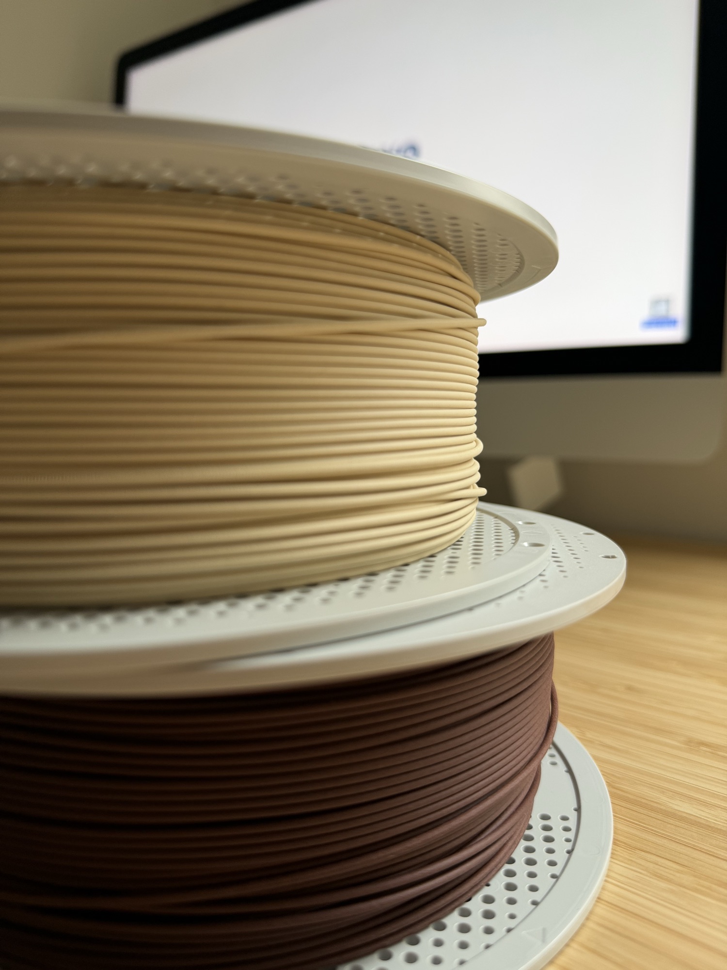 Two spools of 3D-printing filament, beige stacked on brown, on the workshop bench in Cascais.