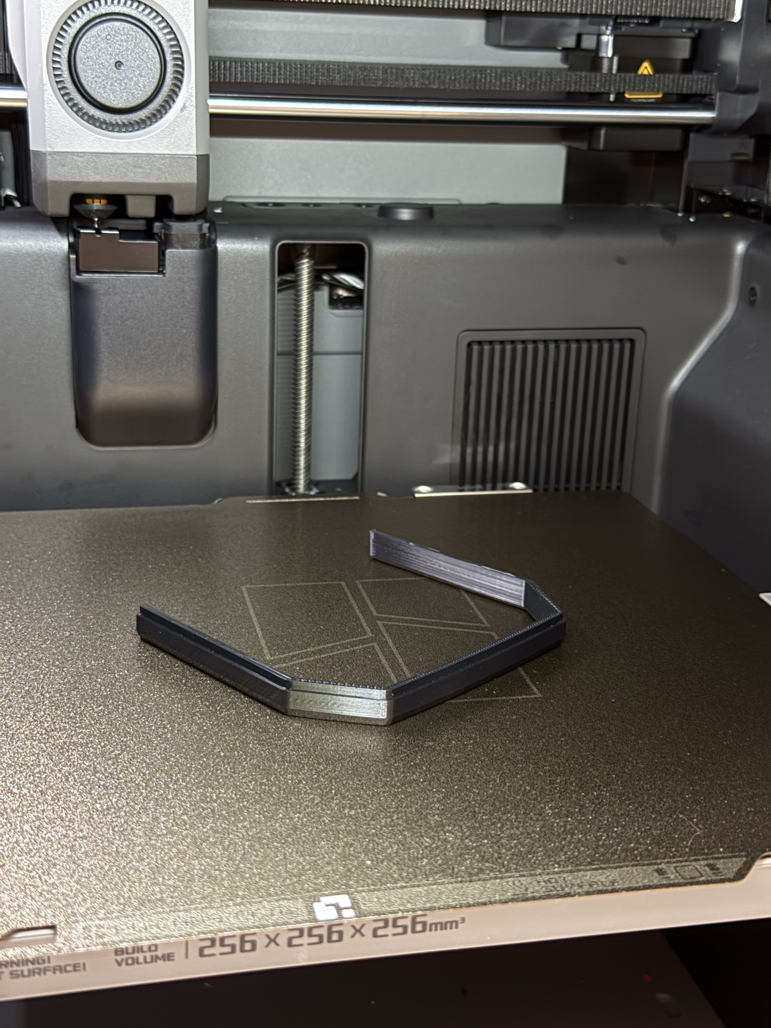A black TPU gasket just printed, still on the build plate inside the 3D printer.