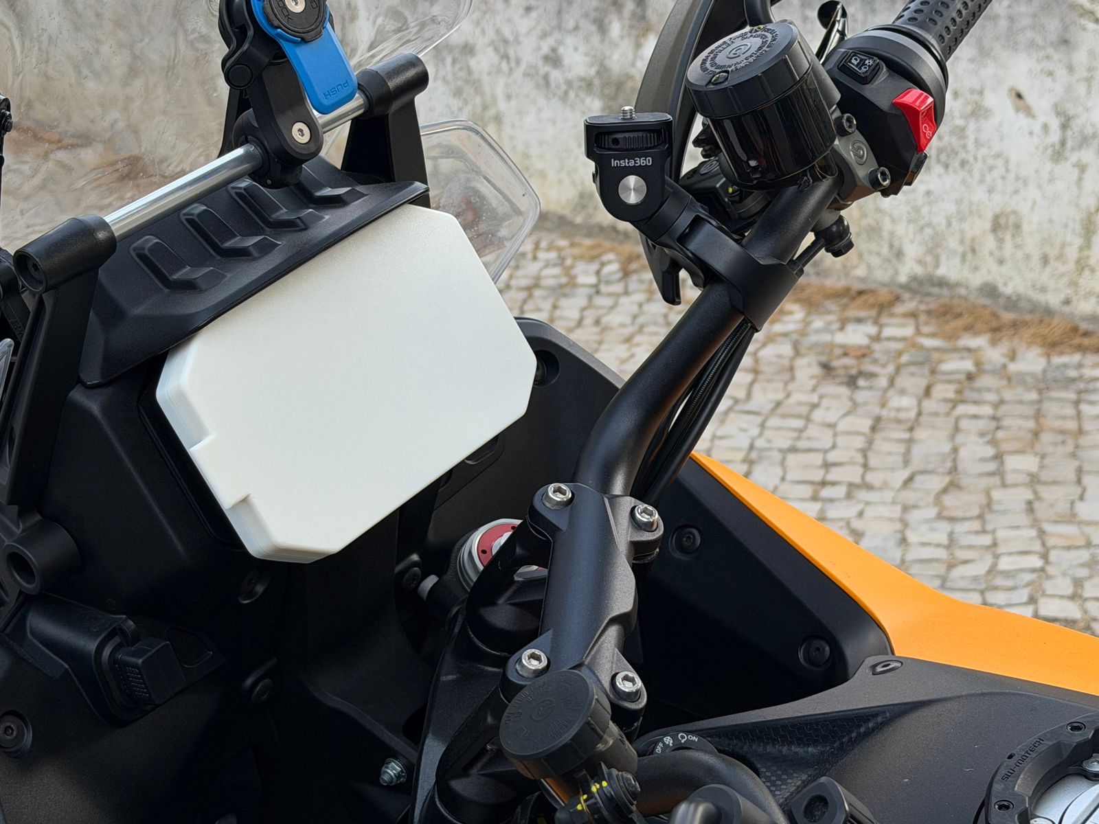 White 3D-printed dash cover fitted over the TFT instrument screen of a Moto Guzzi Stelvio parked in Cascais.