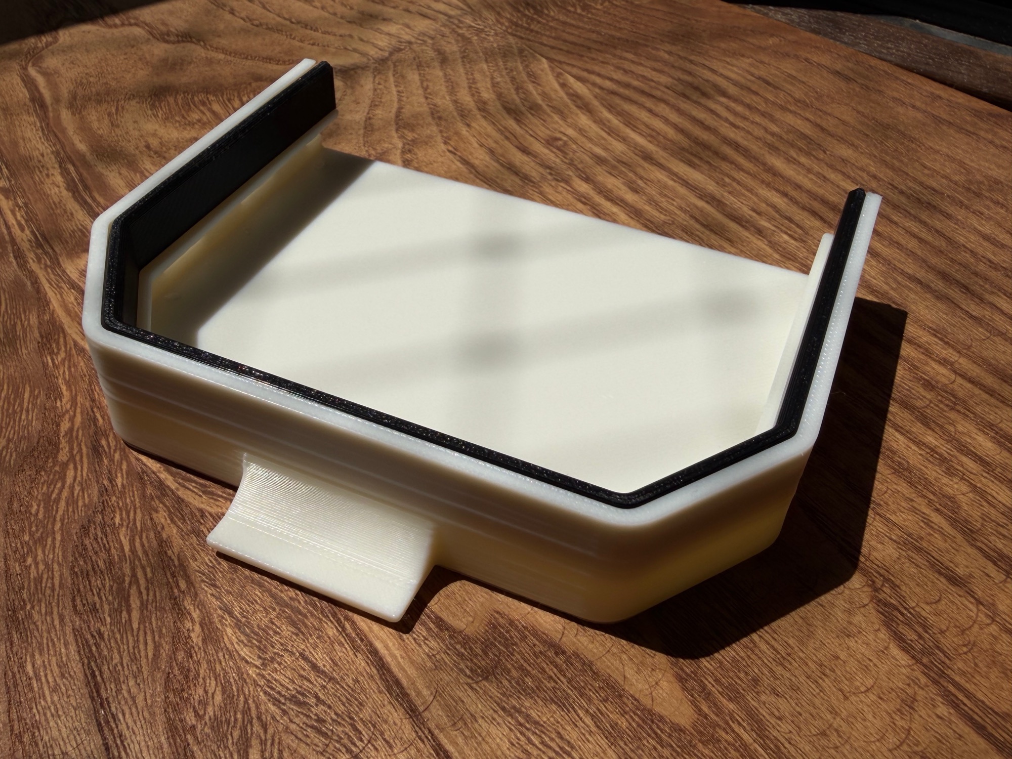 The printed white ASA shell of the dash cover in sunlight, with the black TPU seal frame fitted around the inside and the pull tab at the front.