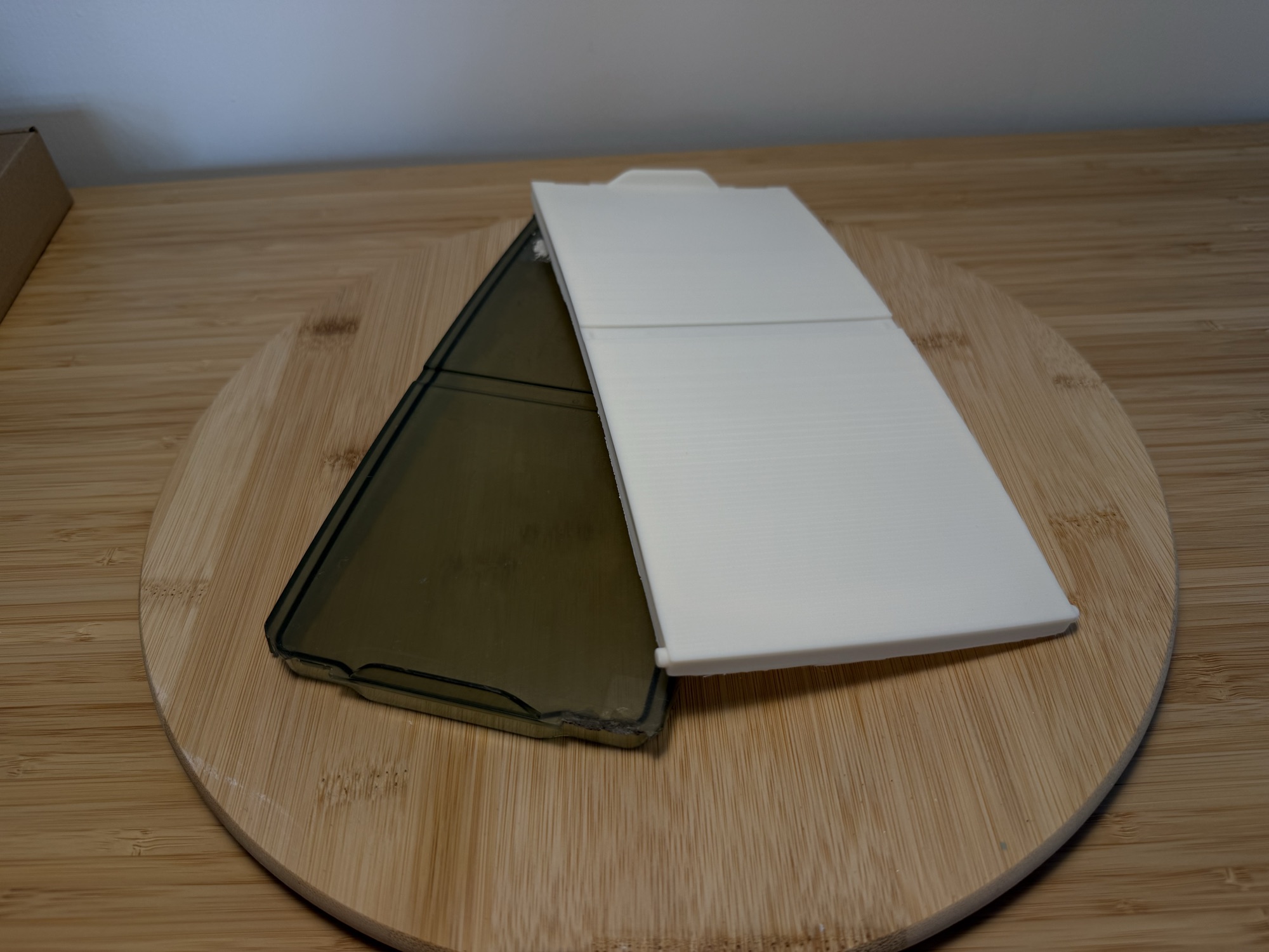 A new white 3D-printed lid for an outdoor pool control box beside the cracked smoked-plastic original.