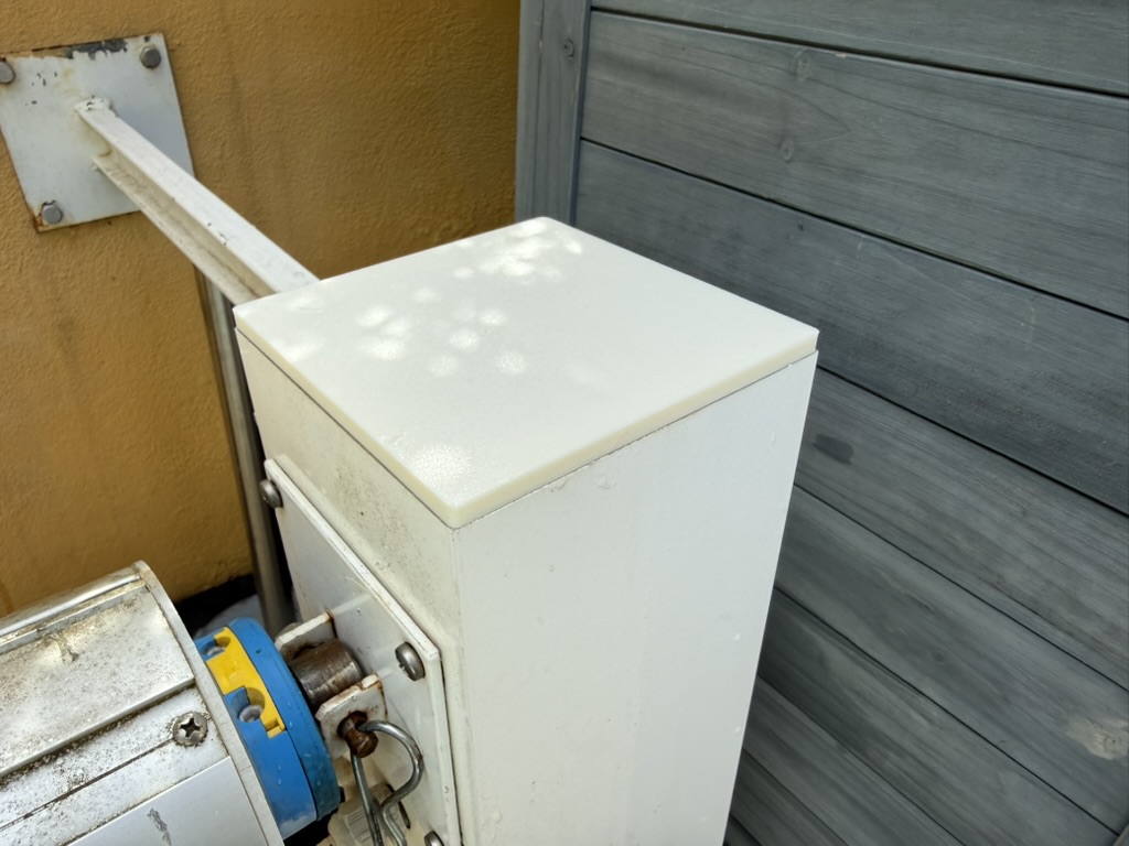 A new white cap fitted on top of a square post of the pool-cover reel, next to the roller and its drive.